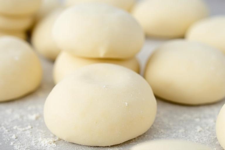 Pile di impasti per pizza freschi e perfettamente lievitati, pronti per la distribuzione professionale.